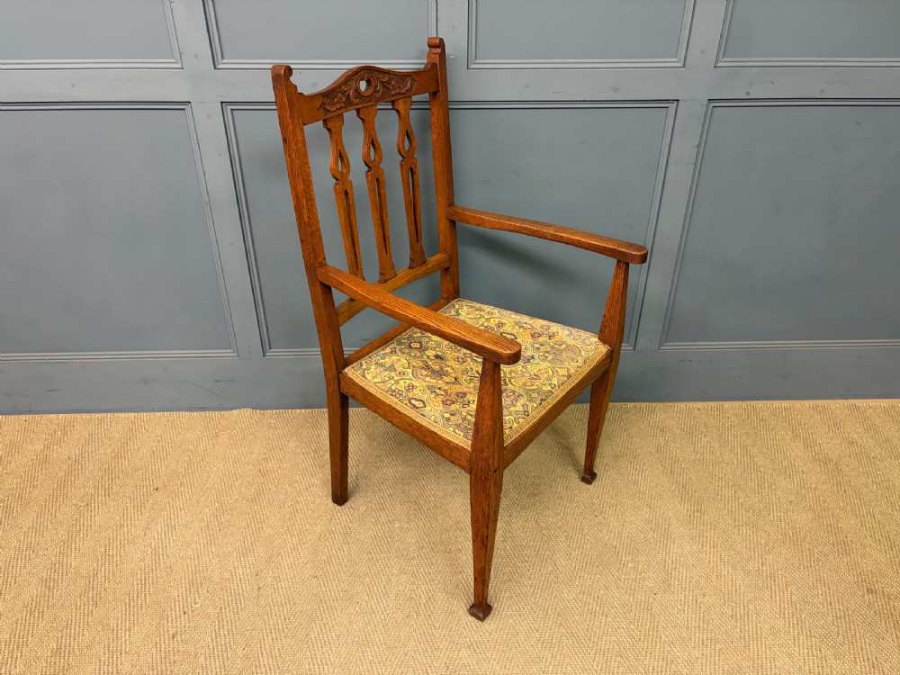 A five-piece Arts and Crafts oak salon suite comprising a two-seater settee, two armchairs, and two side chairs with carved crest rails and patterned upholstery. View XXII