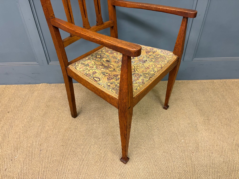 A five-piece Arts and Crafts oak salon suite comprising a two-seater settee, two armchairs, and two side chairs with carved crest rails and patterned upholstery. View XXIII