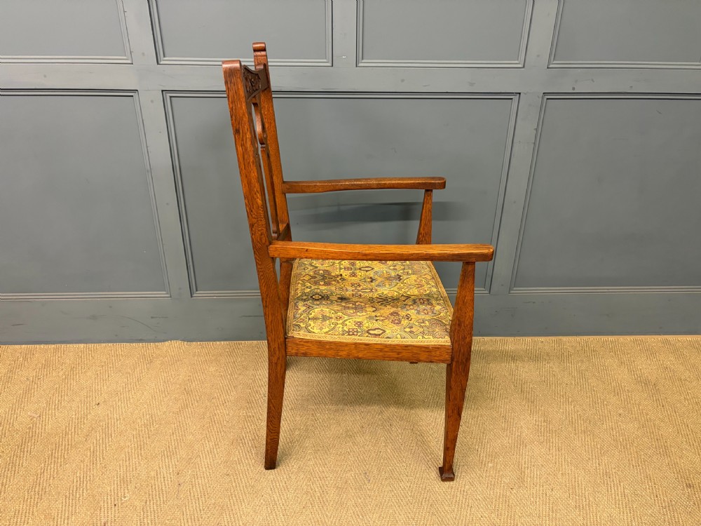 A five-piece Arts and Crafts oak salon suite comprising a two-seater settee, two armchairs, and two side chairs with carved crest rails and patterned upholstery. View XXIV