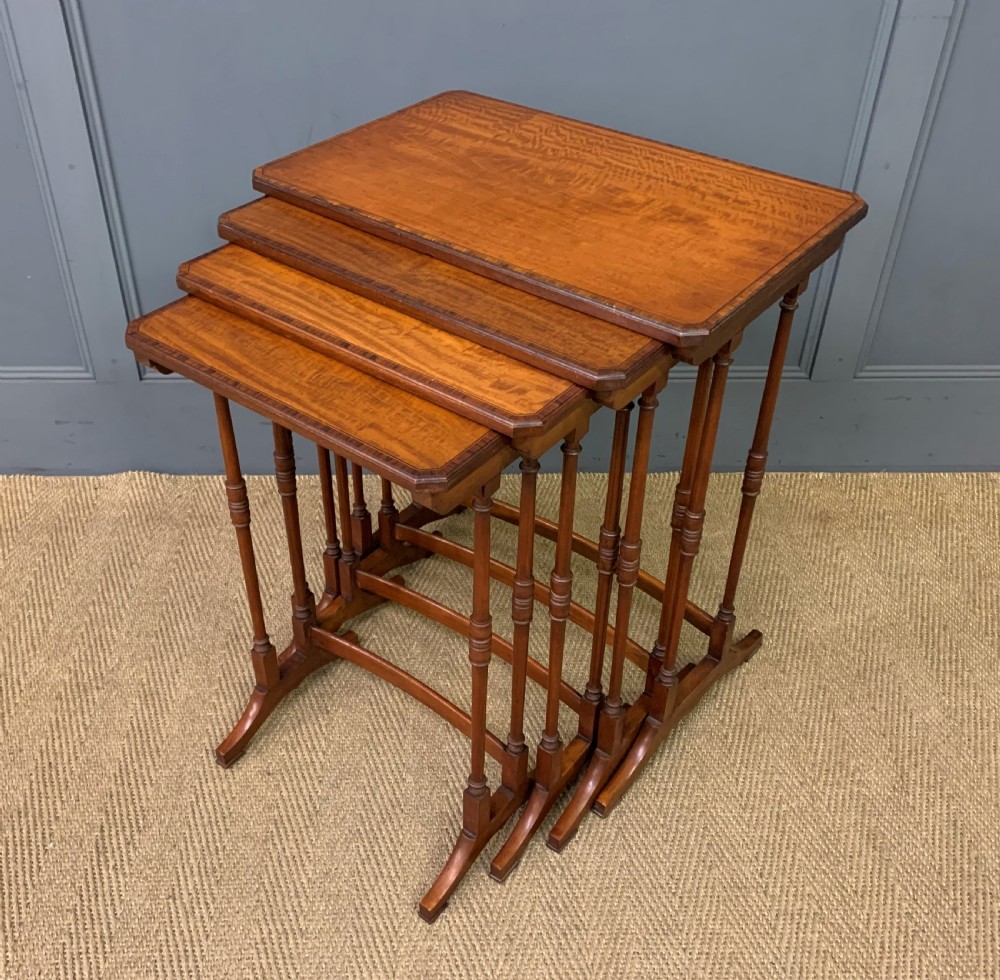 A nest of four graduated wooden tables featuring figure-grained satinwood tops with inlaid borders and slender turned legs.