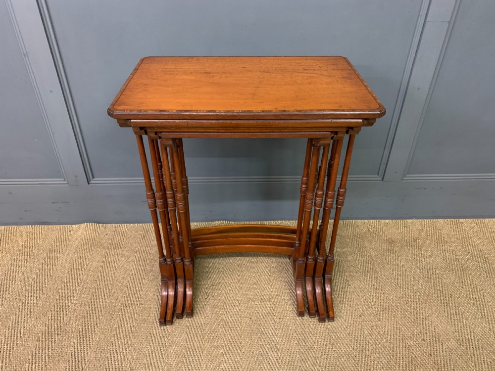 A nest of four graduated wooden tables featuring figure-grained satinwood tops with inlaid borders and slender turned legs. View II