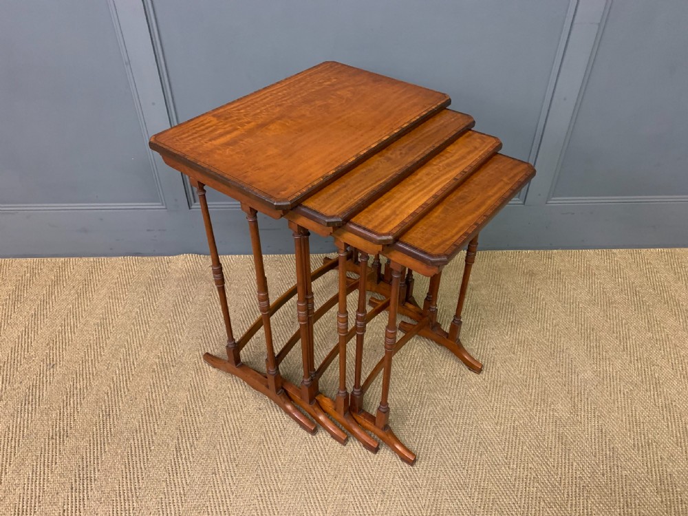 A nest of four graduated wooden tables featuring figure-grained satinwood tops with inlaid borders and slender turned legs. View VIII
