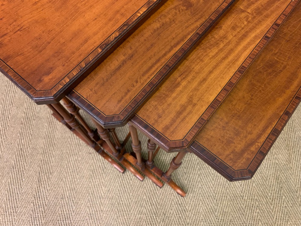 A nest of four graduated wooden tables featuring figure-grained satinwood tops with inlaid borders and slender turned legs. View X