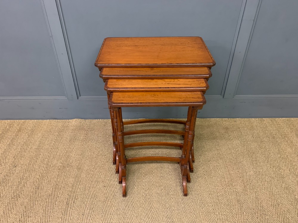 A nest of four graduated wooden tables featuring figure-grained satinwood tops with inlaid borders and slender turned legs. View XII
