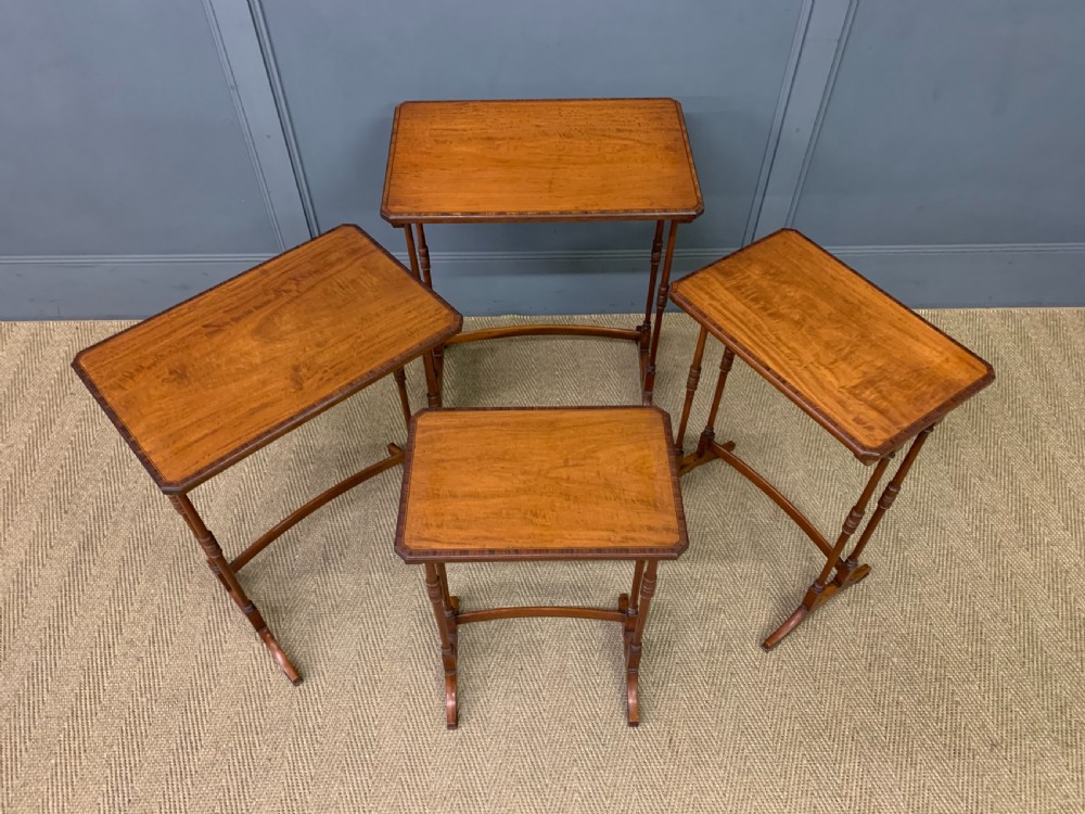 A nest of four graduated wooden tables featuring figure-grained satinwood tops with inlaid borders and slender turned legs. View XIV