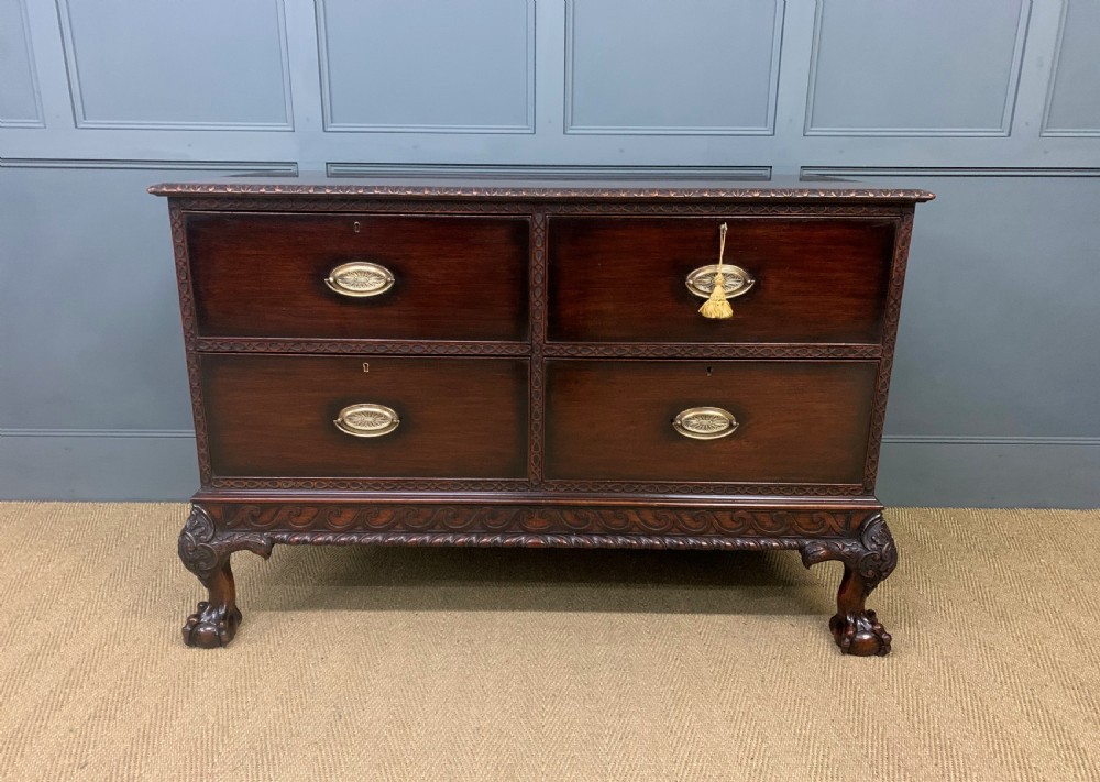 A wide dark mahogany Chippendale style chest featuring four drawers with oval brass handles, carved frieze detailing, and carved ball-and-claw feet. View II