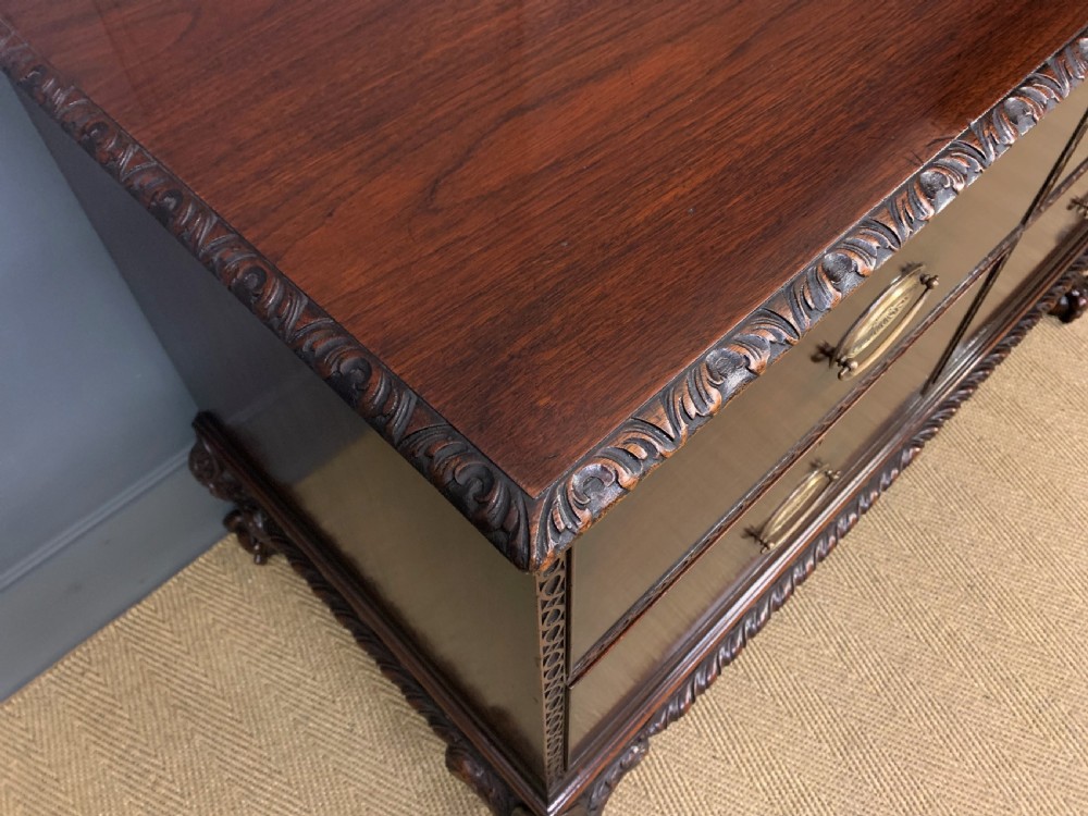 A wide dark mahogany Chippendale style chest featuring four drawers with oval brass handles, carved frieze detailing, and carved ball-and-claw feet. View IV