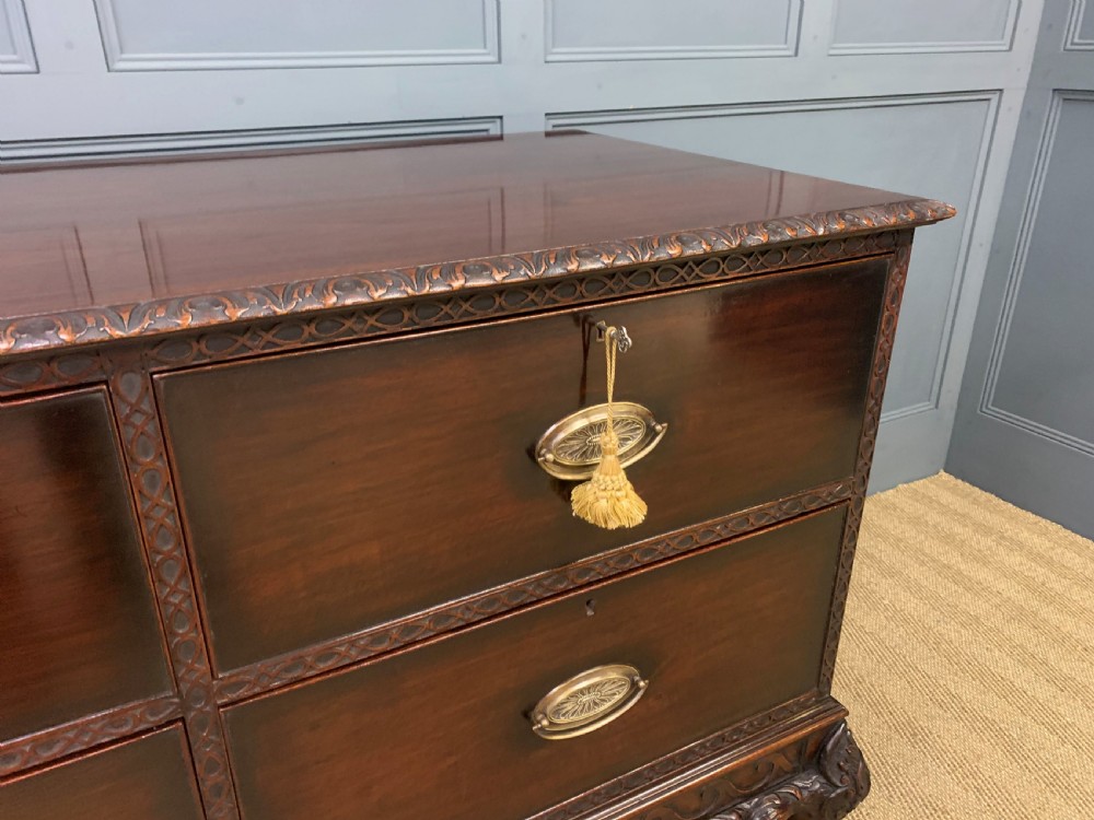 A wide dark mahogany Chippendale style chest featuring four drawers with oval brass handles, carved frieze detailing, and carved ball-and-claw feet. View V