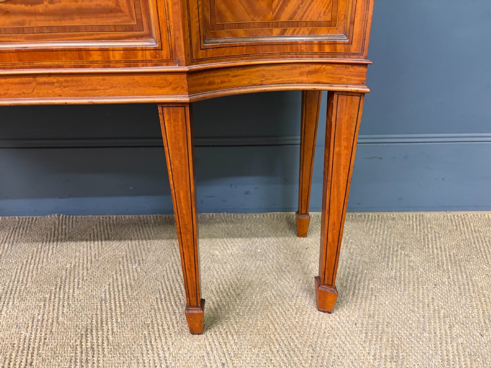 An Edwardian inlaid satinwood display cabinet featuring a central glazed door with an oval wood frame, fabric-lined shelves, and tapered square legs. View VII