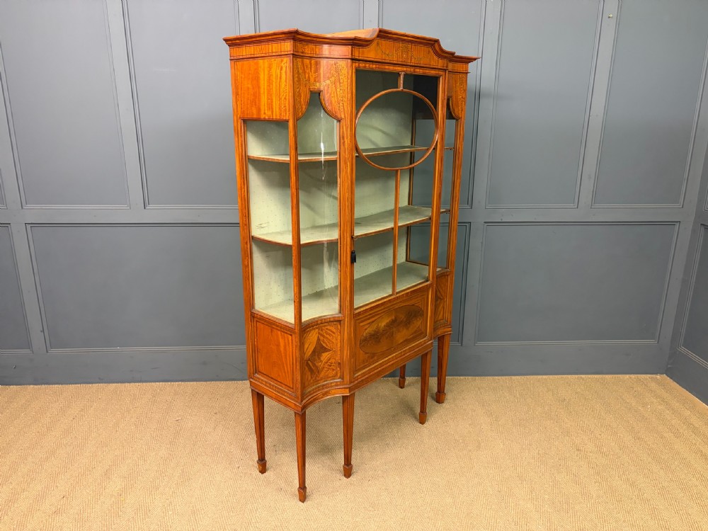 An Edwardian inlaid satinwood display cabinet featuring a central glazed door with an oval wood frame, fabric-lined shelves, and tapered square legs. View XIII