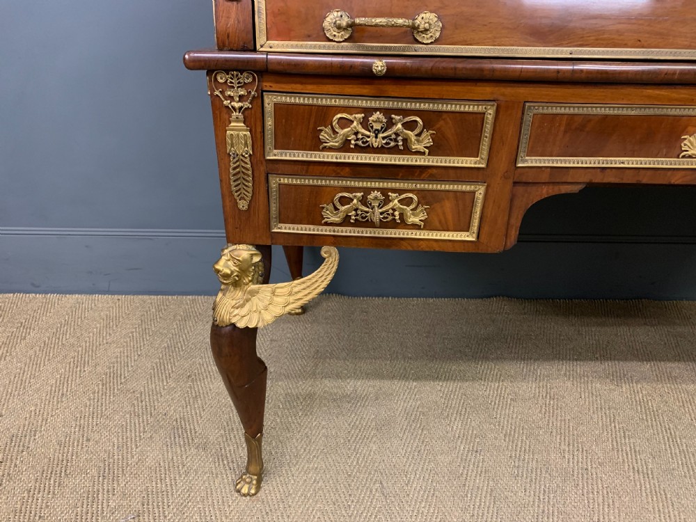 A nineteenth-century French Empire flame mahogany cylinder desk featuring a pink marble top, ornate gilt bronze mounts, and carved winged lion feet. View VII