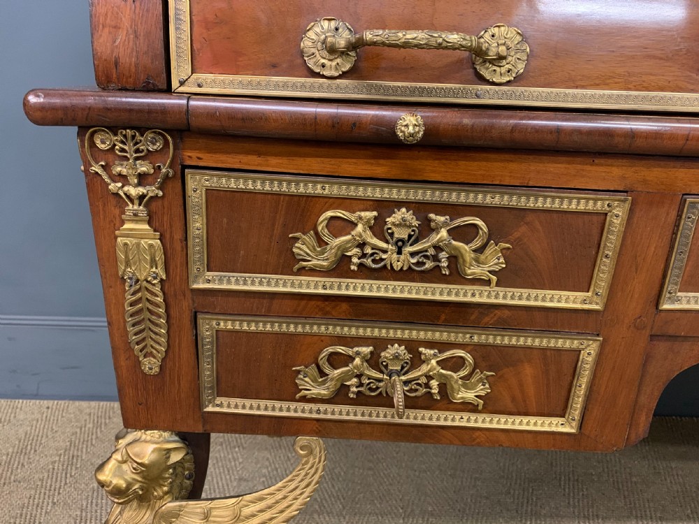 A nineteenth-century French Empire flame mahogany cylinder desk featuring a pink marble top, ornate gilt bronze mounts, and carved winged lion feet. View VIII