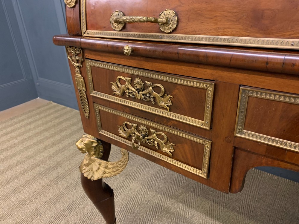 A nineteenth-century French Empire flame mahogany cylinder desk featuring a pink marble top, ornate gilt bronze mounts, and carved winged lion feet. View IX