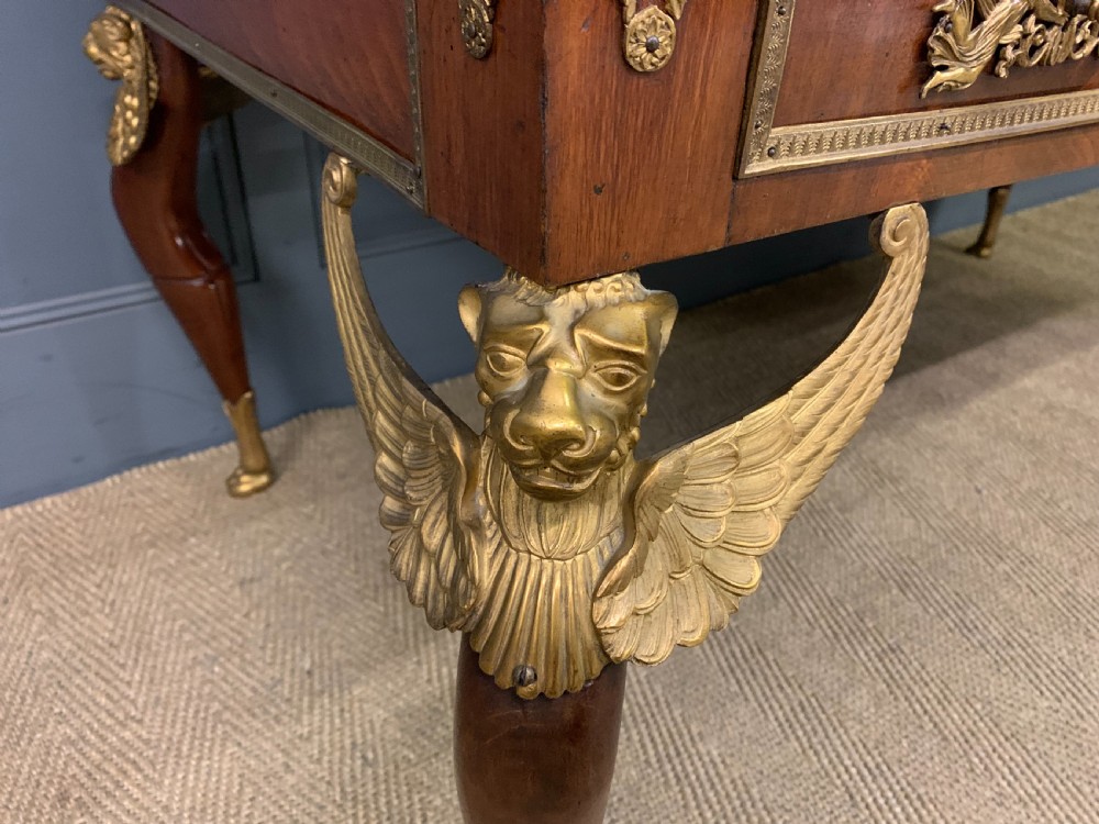 A nineteenth-century French Empire flame mahogany cylinder desk featuring a pink marble top, ornate gilt bronze mounts, and carved winged lion feet. View X