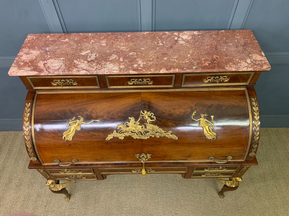 A nineteenth-century French Empire flame mahogany cylinder desk featuring a pink marble top, ornate gilt bronze mounts, and carved winged lion feet. View XIII