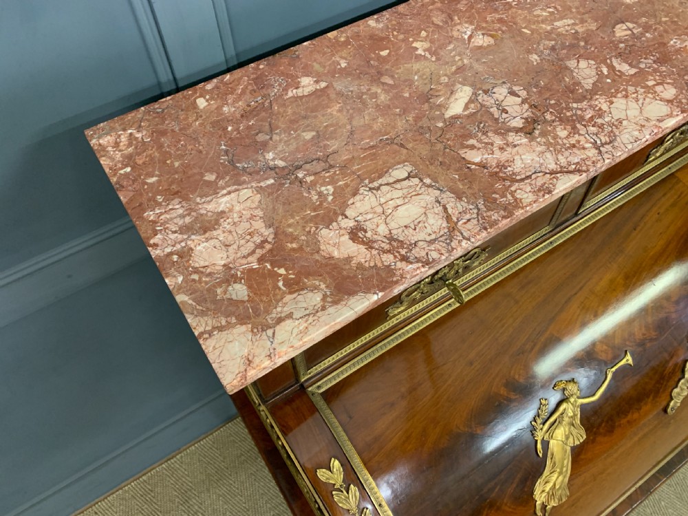 A nineteenth-century French Empire flame mahogany cylinder desk featuring a pink marble top, ornate gilt bronze mounts, and carved winged lion feet. View XIV