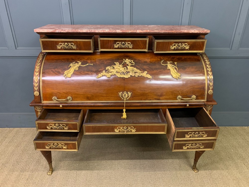 A nineteenth-century French Empire flame mahogany cylinder desk featuring a pink marble top, ornate gilt bronze mounts, and carved winged lion feet. View XV