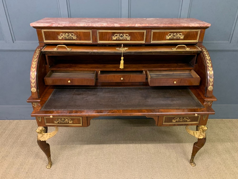 A nineteenth-century French Empire flame mahogany cylinder desk featuring a pink marble top, ornate gilt bronze mounts, and carved winged lion feet. View XVII