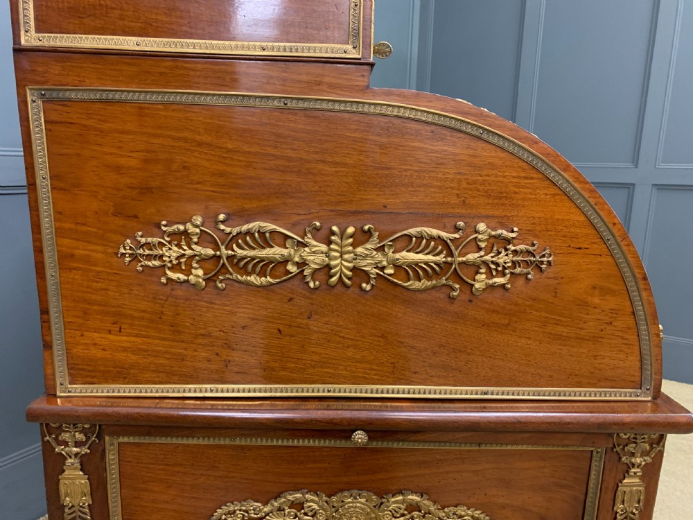 A nineteenth-century French Empire flame mahogany cylinder desk featuring a pink marble top, ornate gilt bronze mounts, and carved winged lion feet. View XX