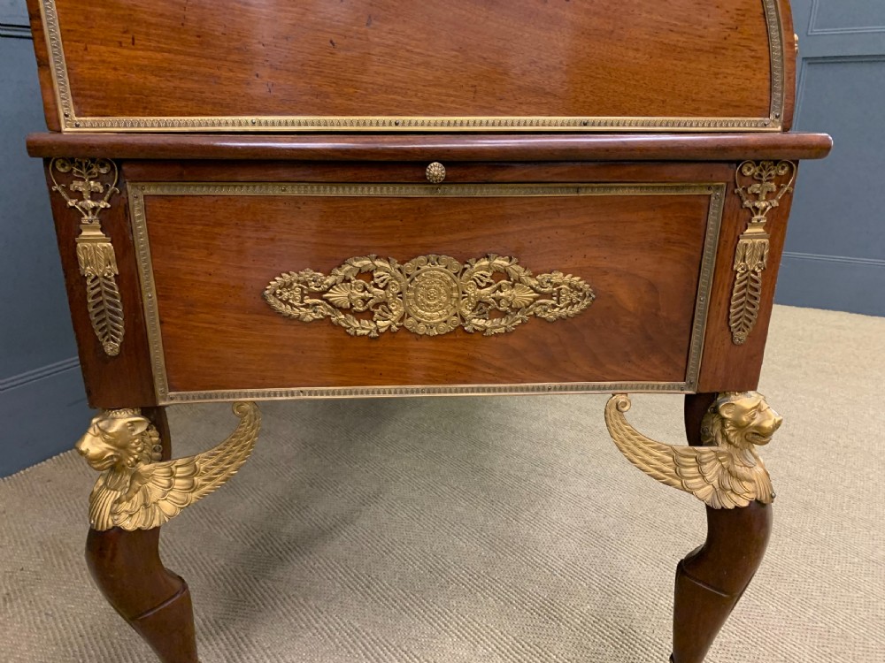 A nineteenth-century French Empire flame mahogany cylinder desk featuring a pink marble top, ornate gilt bronze mounts, and carved winged lion feet. View XXI