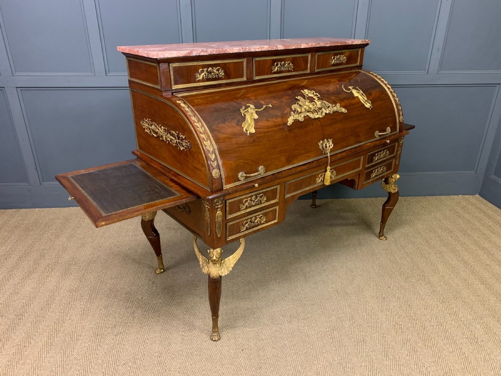 A nineteenth-century French Empire flame mahogany cylinder desk featuring a pink marble top, ornate gilt bronze mounts, and carved winged lion feet. View XXII