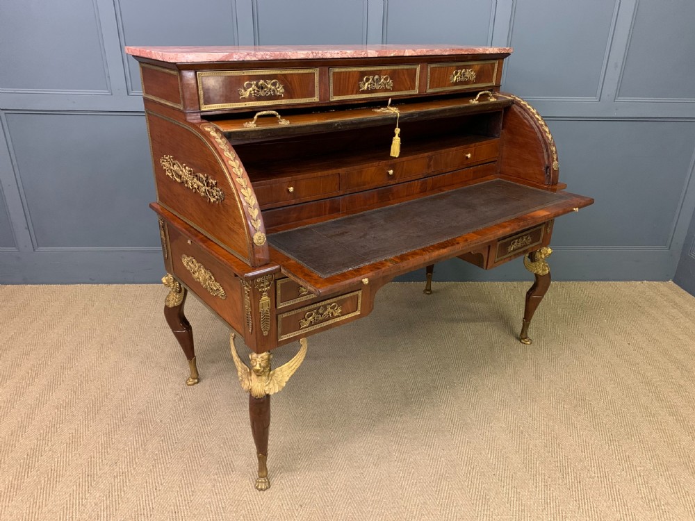A nineteenth-century French Empire flame mahogany cylinder desk featuring a pink marble top, ornate gilt bronze mounts, and carved winged lion feet. View XXIII