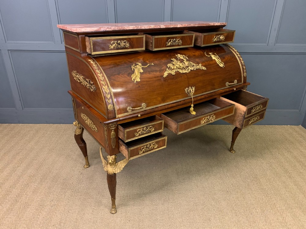 A nineteenth-century French Empire flame mahogany cylinder desk featuring a pink marble top, ornate gilt bronze mounts, and carved winged lion feet. View XXIV