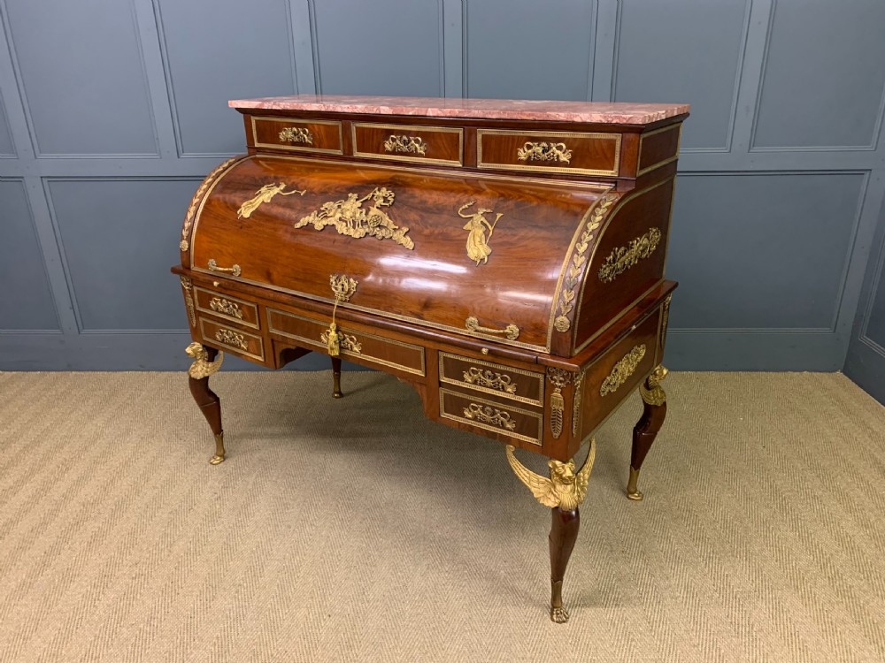 A nineteenth-century French Empire flame mahogany cylinder desk featuring a pink marble top, ornate gilt bronze mounts, and carved winged lion feet. View XXV