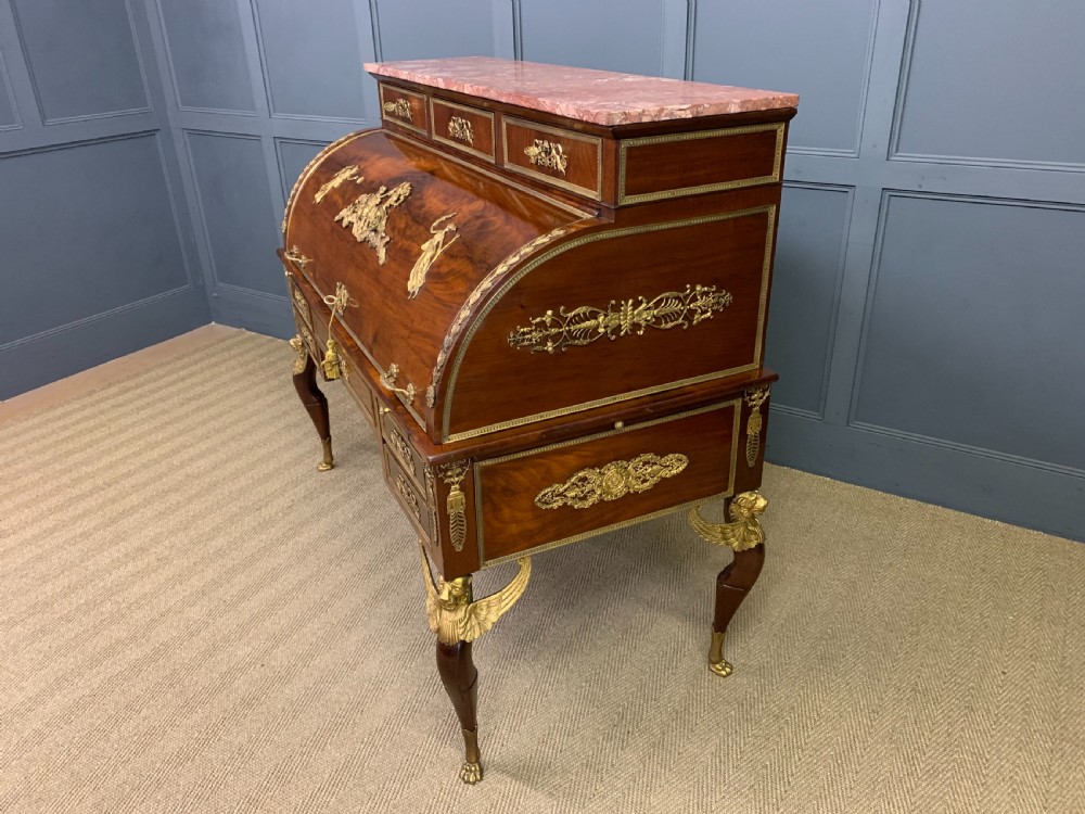 A nineteenth-century French Empire flame mahogany cylinder desk featuring a pink marble top, ornate gilt bronze mounts, and carved winged lion feet. View XXVI