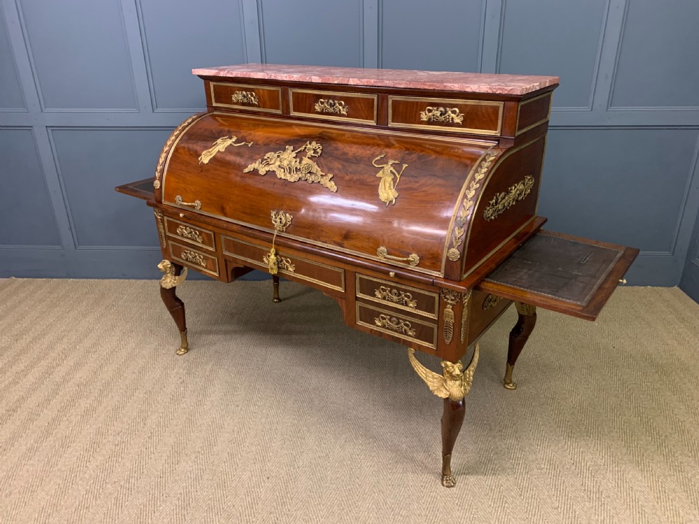 A nineteenth-century French Empire flame mahogany cylinder desk featuring a pink marble top, ornate gilt bronze mounts, and carved winged lion feet. View XXVII
