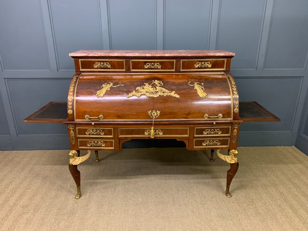 A nineteenth-century French Empire flame mahogany cylinder desk featuring a pink marble top, ornate gilt bronze mounts, and carved winged lion feet. View XXVIII