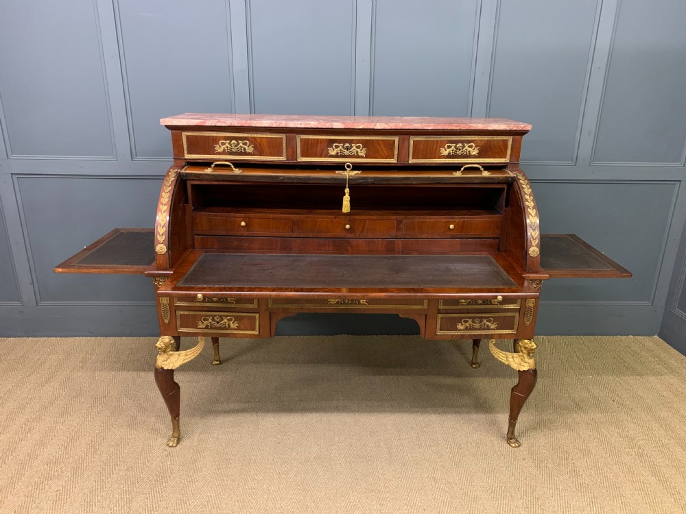 A nineteenth-century French Empire flame mahogany cylinder desk featuring a pink marble top, ornate gilt bronze mounts, and carved winged lion feet. View XXIX