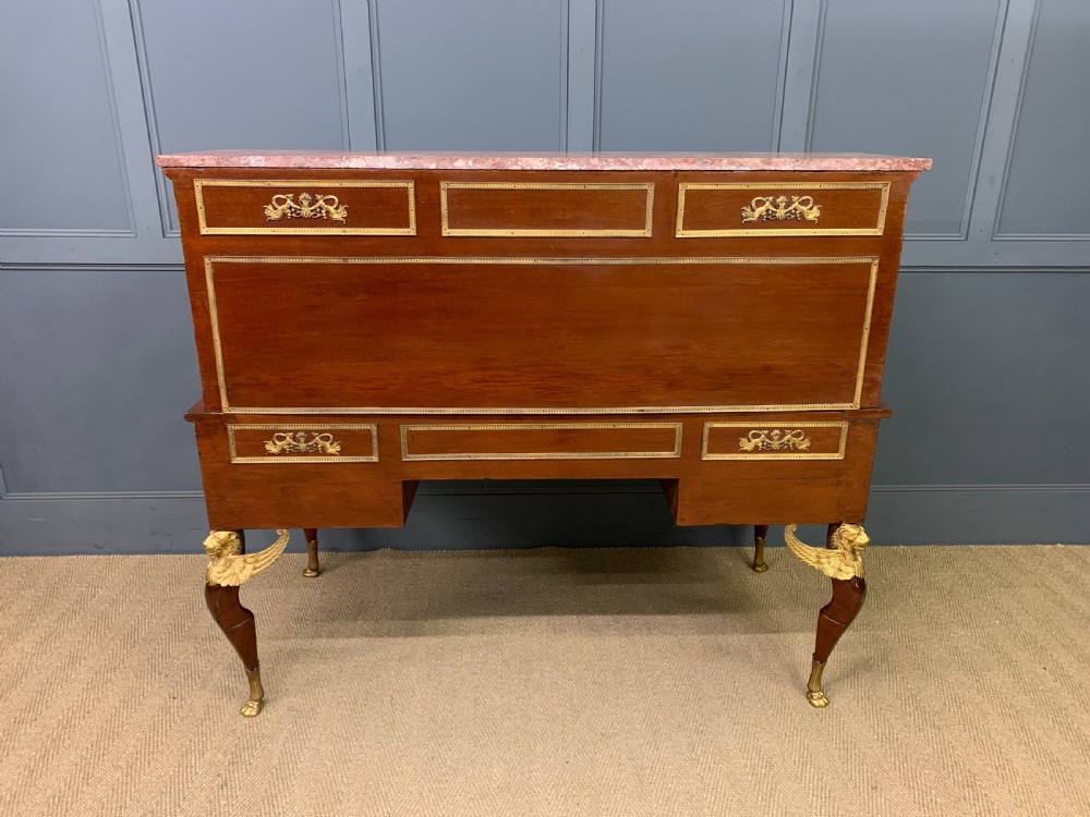 A nineteenth-century French Empire flame mahogany cylinder desk featuring a pink marble top, ornate gilt bronze mounts, and carved winged lion feet. View XXX