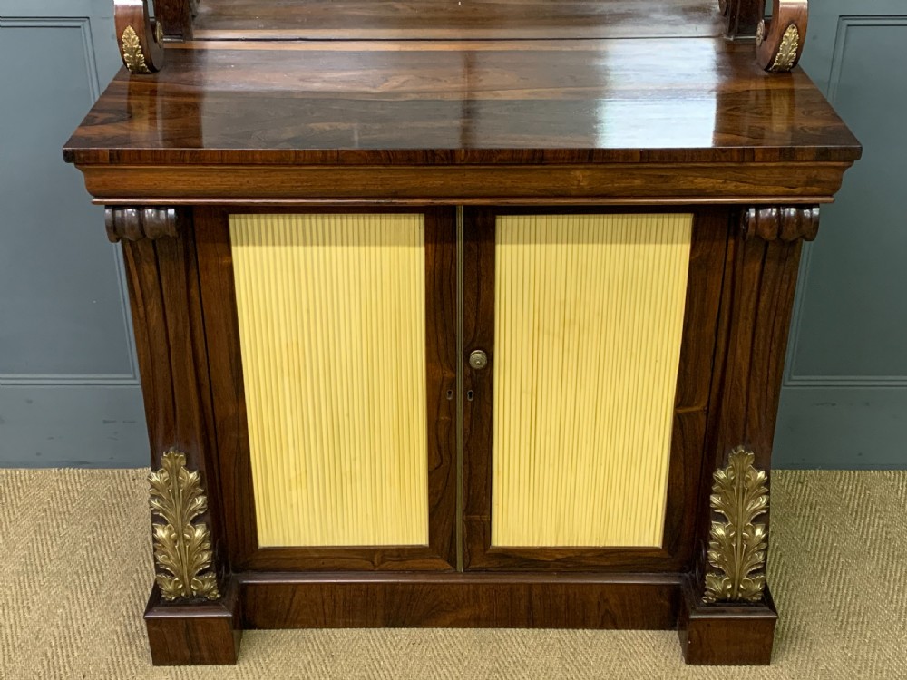 A Regency rosewood chiffonier cabinet featuring a top shelf with a brass gallery on S-scroll supports over a two-door cupboard with pleated yellow fabric panels. View V