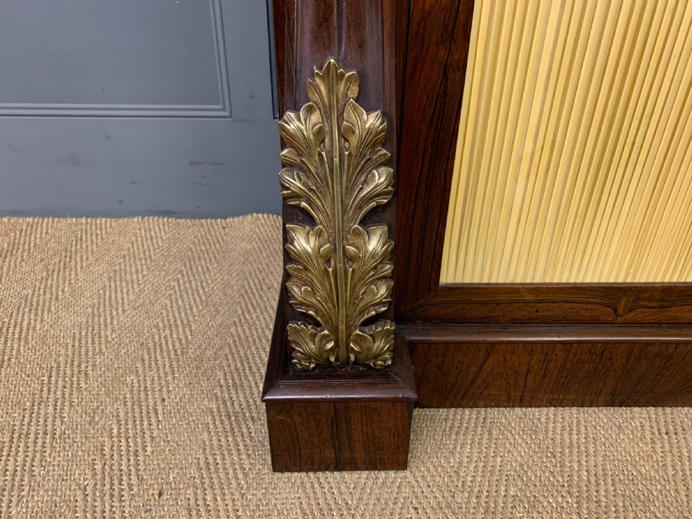 A Regency rosewood chiffonier cabinet featuring a top shelf with a brass gallery on S-scroll supports over a two-door cupboard with pleated yellow fabric panels. View VIII