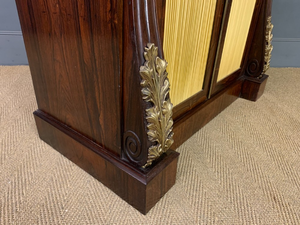 A Regency rosewood chiffonier cabinet featuring a top shelf with a brass gallery on S-scroll supports over a two-door cupboard with pleated yellow fabric panels. View IX