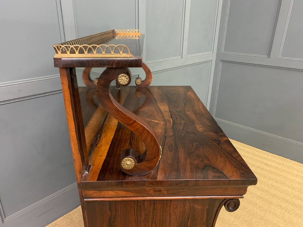 A Regency rosewood chiffonier cabinet featuring a top shelf with a brass gallery on S-scroll supports over a two-door cupboard with pleated yellow fabric panels. View XV