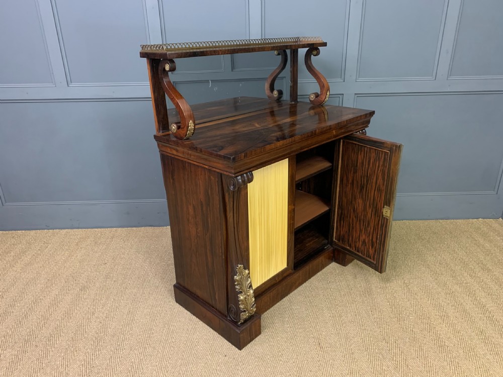 A Regency rosewood chiffonier cabinet featuring a top shelf with a brass gallery on S-scroll supports over a two-door cupboard with pleated yellow fabric panels. View XVII
