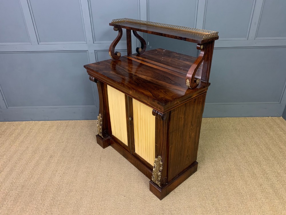 A Regency rosewood chiffonier cabinet featuring a top shelf with a brass gallery on S-scroll supports over a two-door cupboard with pleated yellow fabric panels. View XVIII