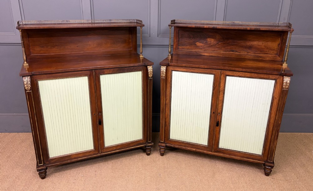 A pair of Regency period rosewood side cabinets featuring brass galleries, raised upper shelves, and pleated light green fabric door panels.