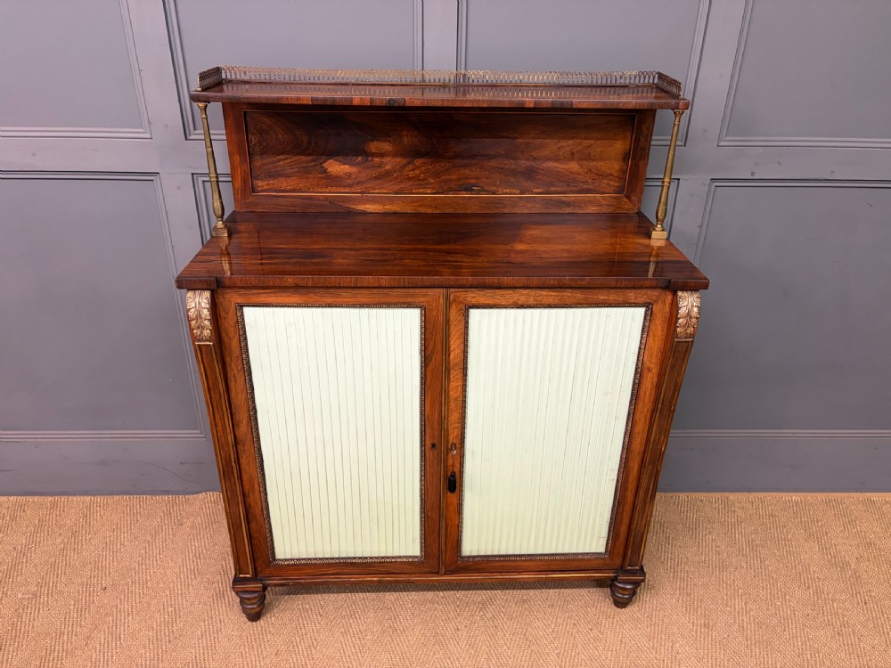 A pair of Regency period rosewood side cabinets featuring brass galleries, raised upper shelves, and pleated light green fabric door panels. View II