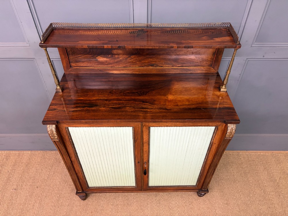 A pair of Regency period rosewood side cabinets featuring brass galleries, raised upper shelves, and pleated light green fabric door panels. View III