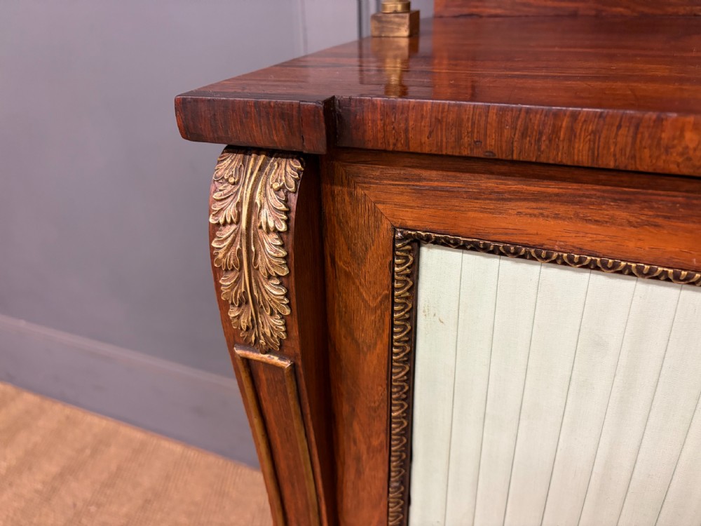 A pair of Regency period rosewood side cabinets featuring brass galleries, raised upper shelves, and pleated light green fabric door panels. View IV