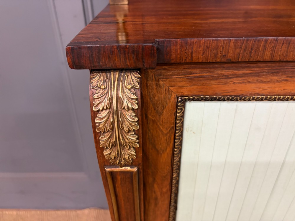 A pair of Regency period rosewood side cabinets featuring brass galleries, raised upper shelves, and pleated light green fabric door panels. View V