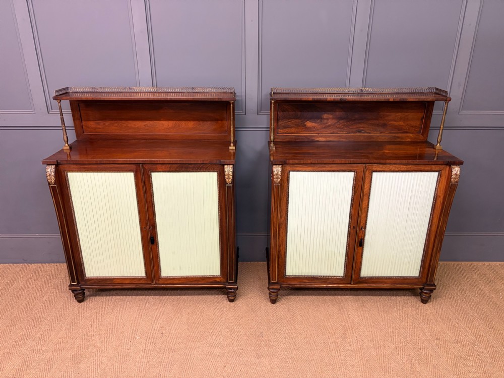 A pair of Regency period rosewood side cabinets featuring brass galleries, raised upper shelves, and pleated light green fabric door panels. View X