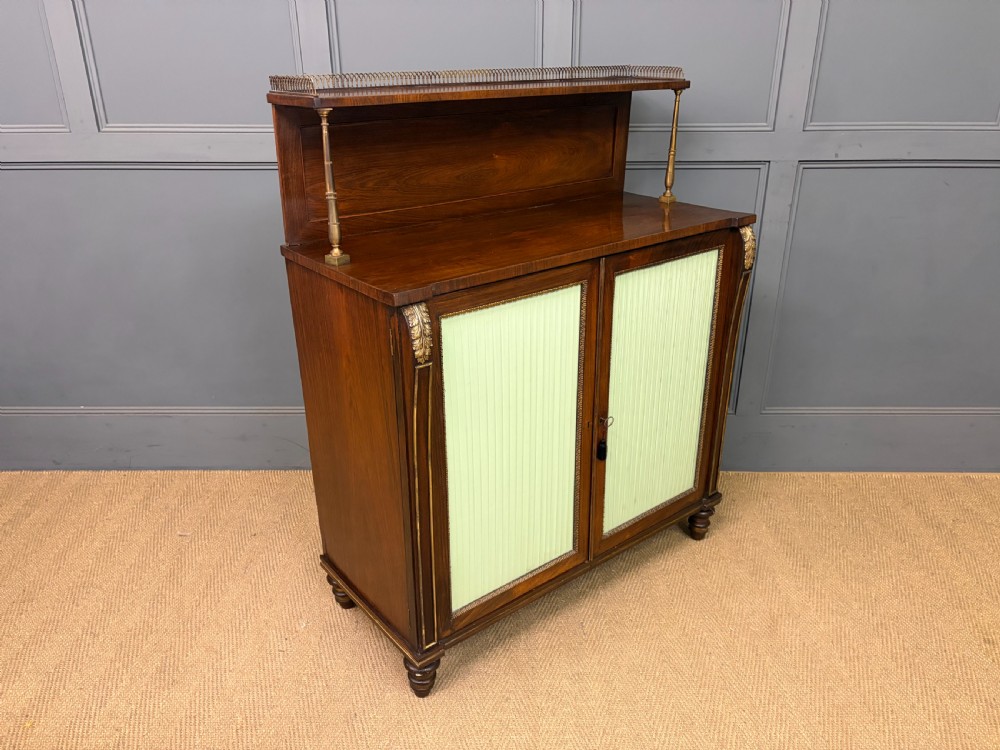 A pair of Regency period rosewood side cabinets featuring brass galleries, raised upper shelves, and pleated light green fabric door panels. View XVI