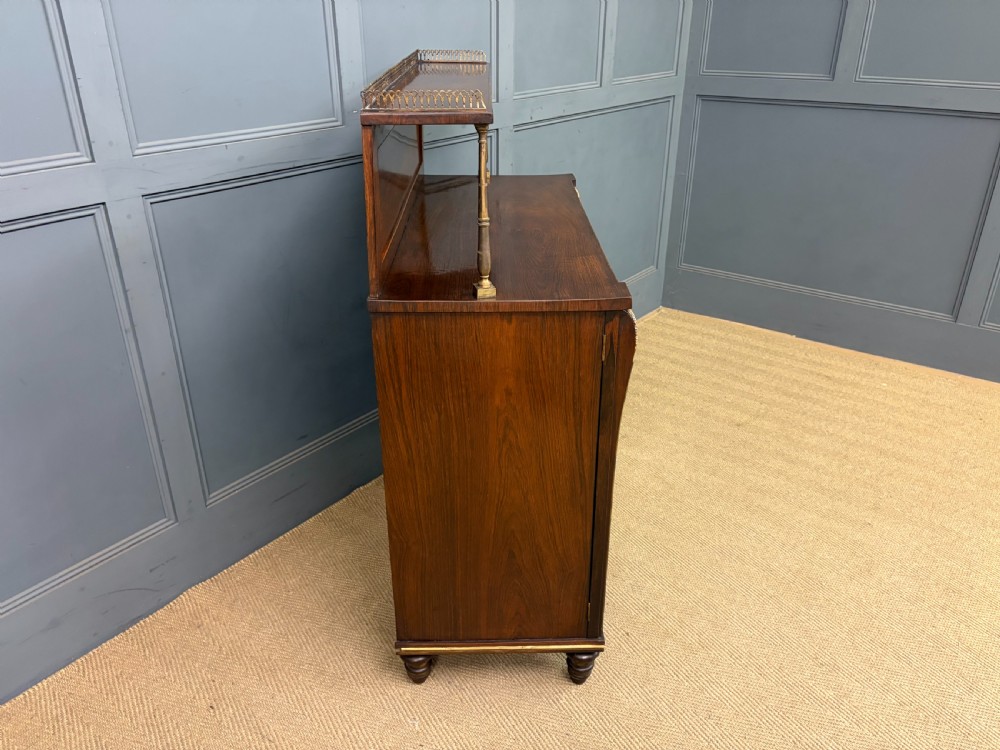 A pair of Regency period rosewood side cabinets featuring brass galleries, raised upper shelves, and pleated light green fabric door panels. View XVII