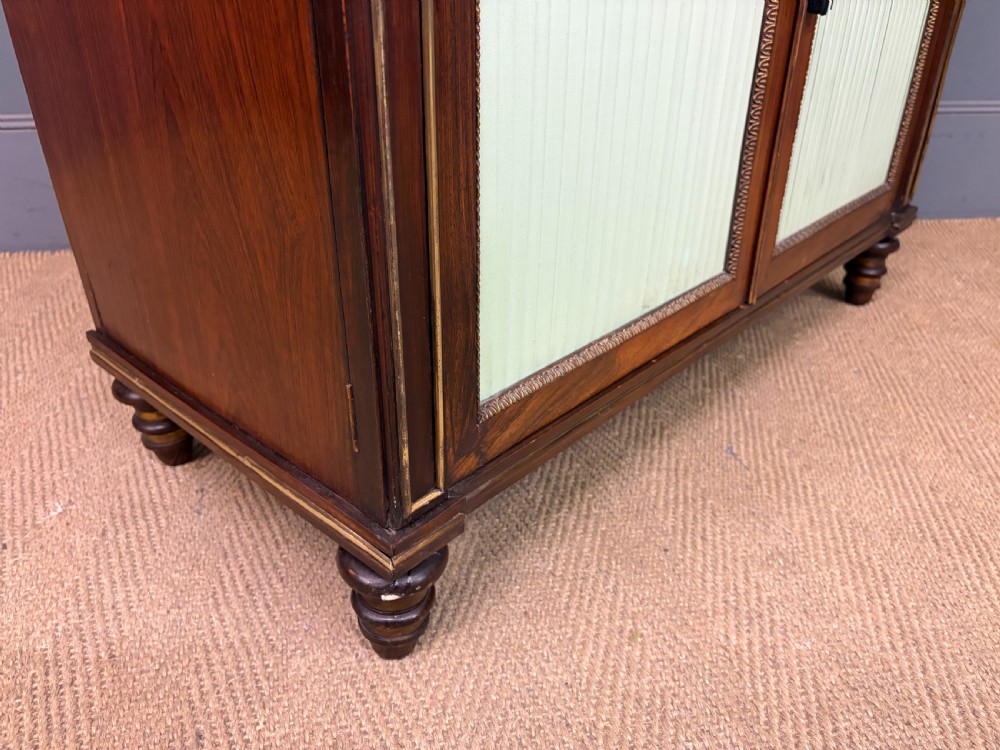 A pair of Regency period rosewood side cabinets featuring brass galleries, raised upper shelves, and pleated light green fabric door panels. View XX