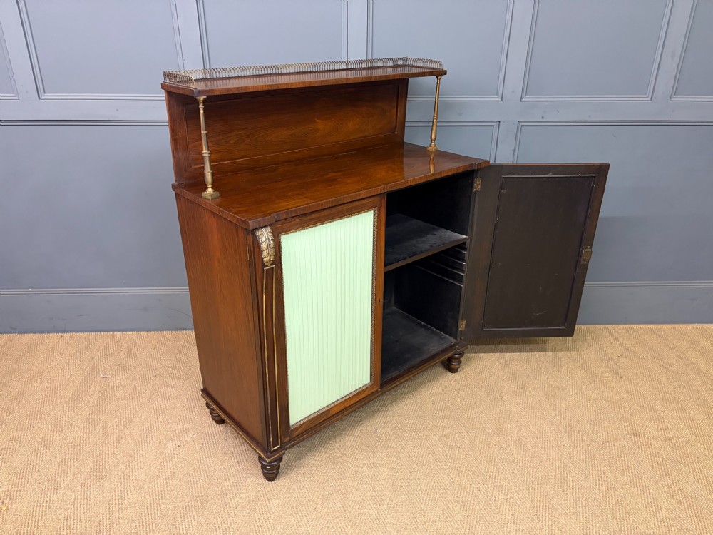 A pair of Regency period rosewood side cabinets featuring brass galleries, raised upper shelves, and pleated light green fabric door panels. View XXI