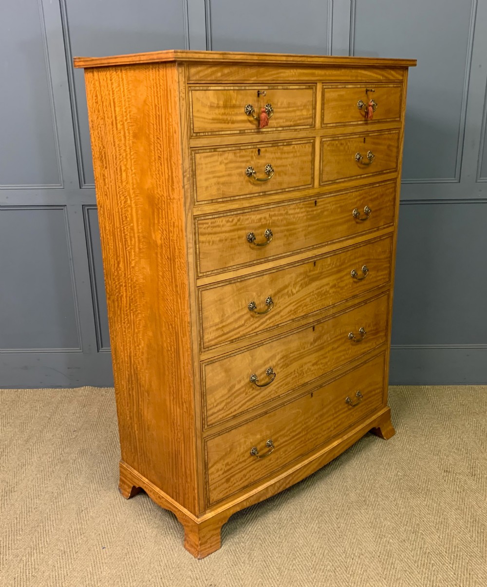 A tall satinwood chest of drawers featuring eight inlaid drawers with brass swan-neck handles and bracket feet.